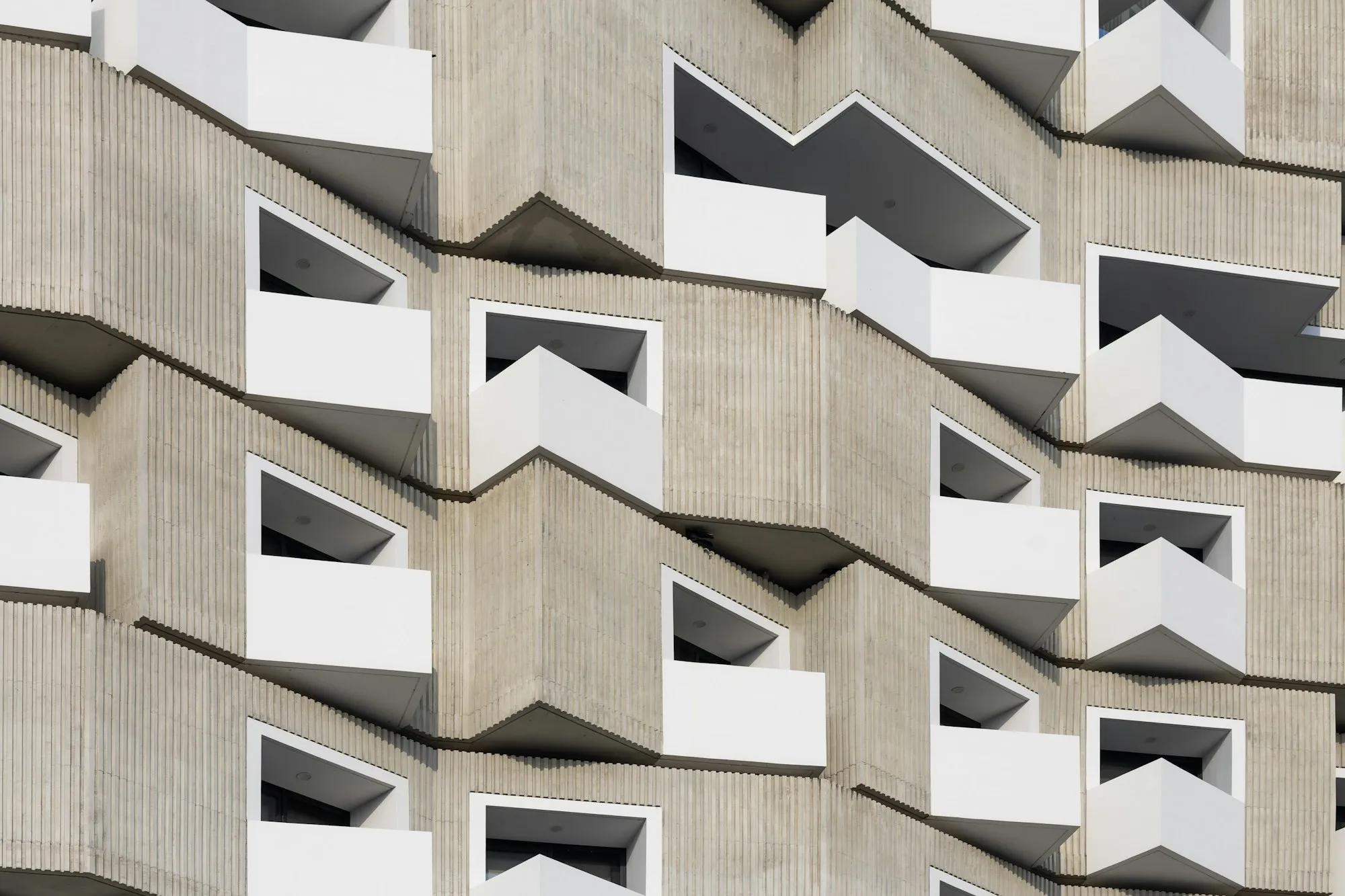 Fachada de hormigón con balcones blancos repetidos en un patrón geométrico modular.
