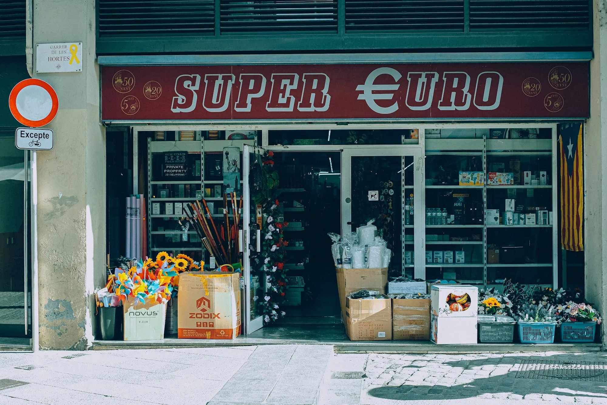 Fachada de un pequeño comercio de barrio en una calle española, con el género expuesto en cajas sobre la acera.